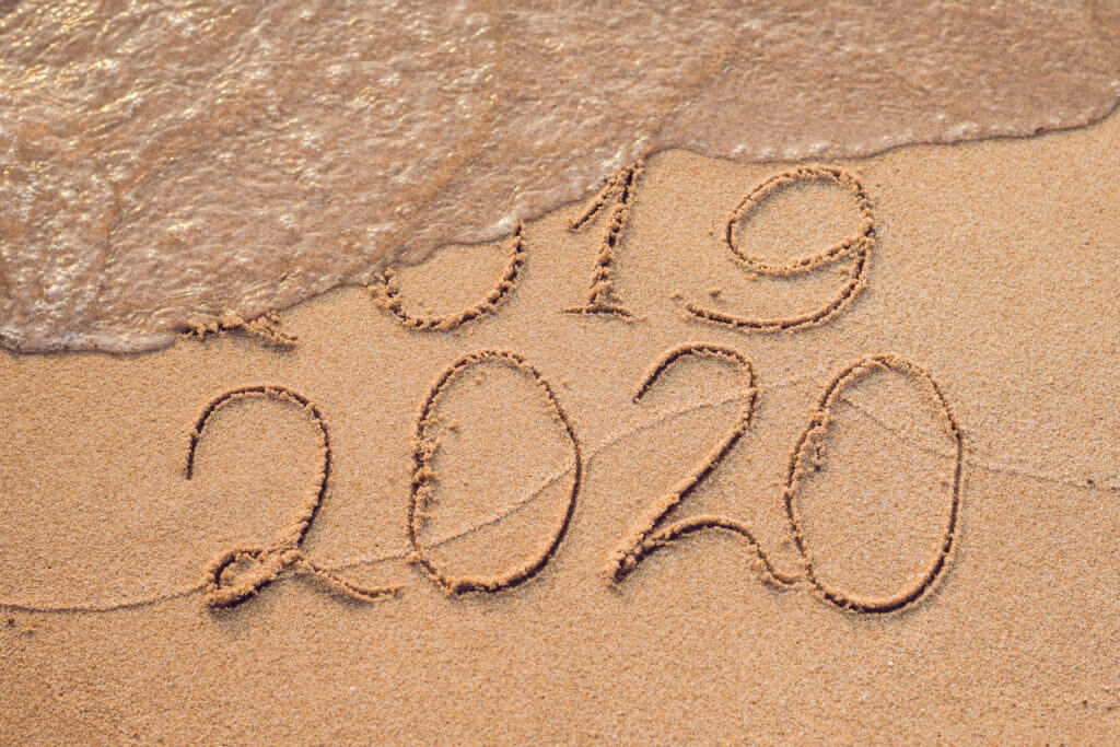 New Year 2020 is coming concept – inscription 2019 and 2020 a beach sand, the wave is almost covering the digits 2019