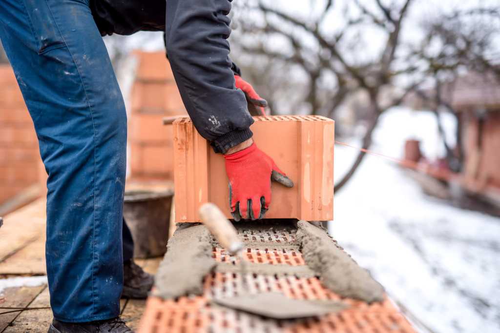 construction site and mason bricklayer working with bricks, cement and mortar for building new house